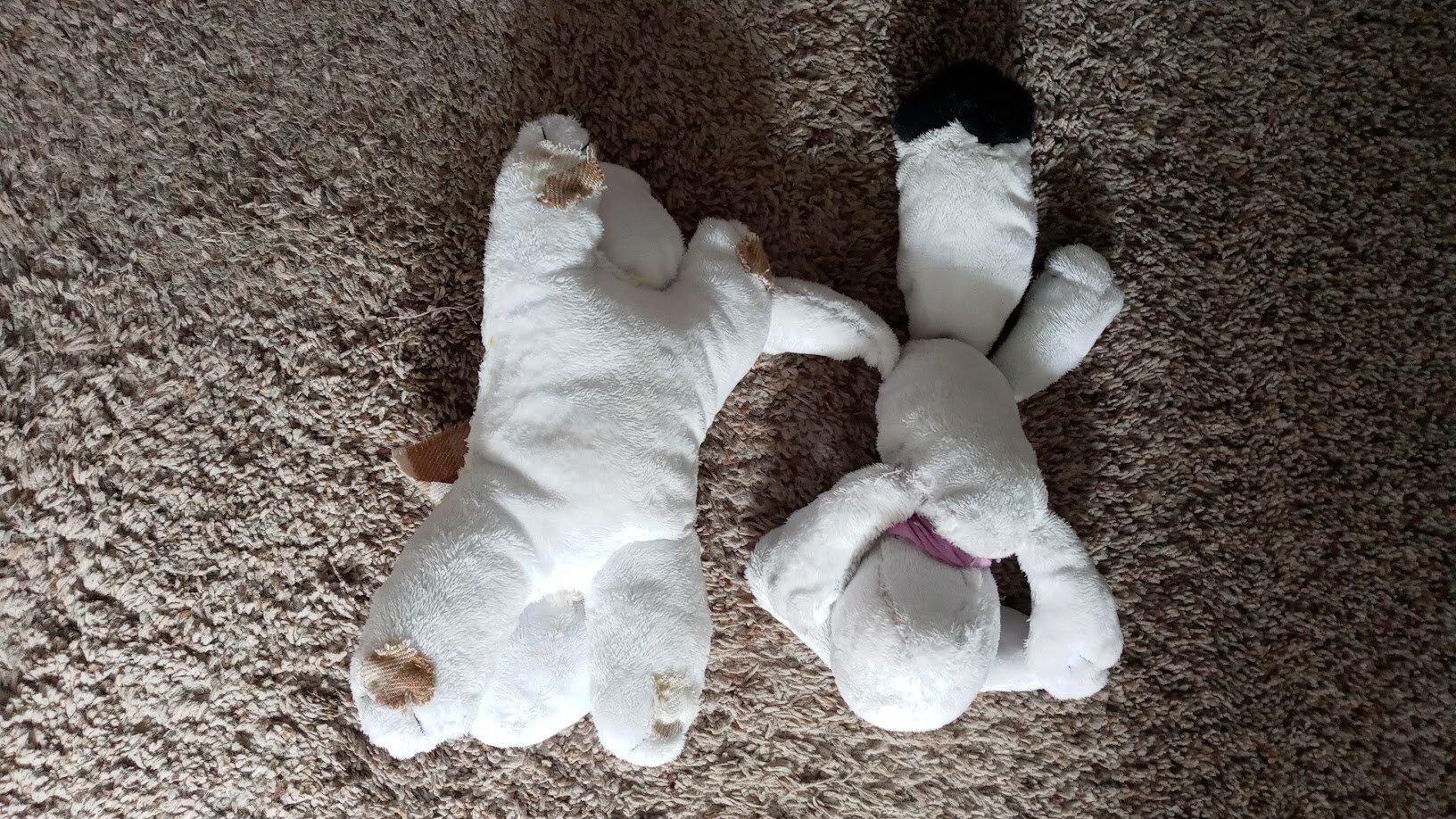 the two plushies again in the same location, flopped upside down. the first one has pawpads sewn roughly on, while the other doesn't. the second one has better-defined legs and flops out in a silly way